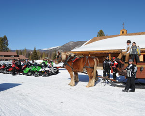snowmobilers outside a lodge with a horse-drawn sled